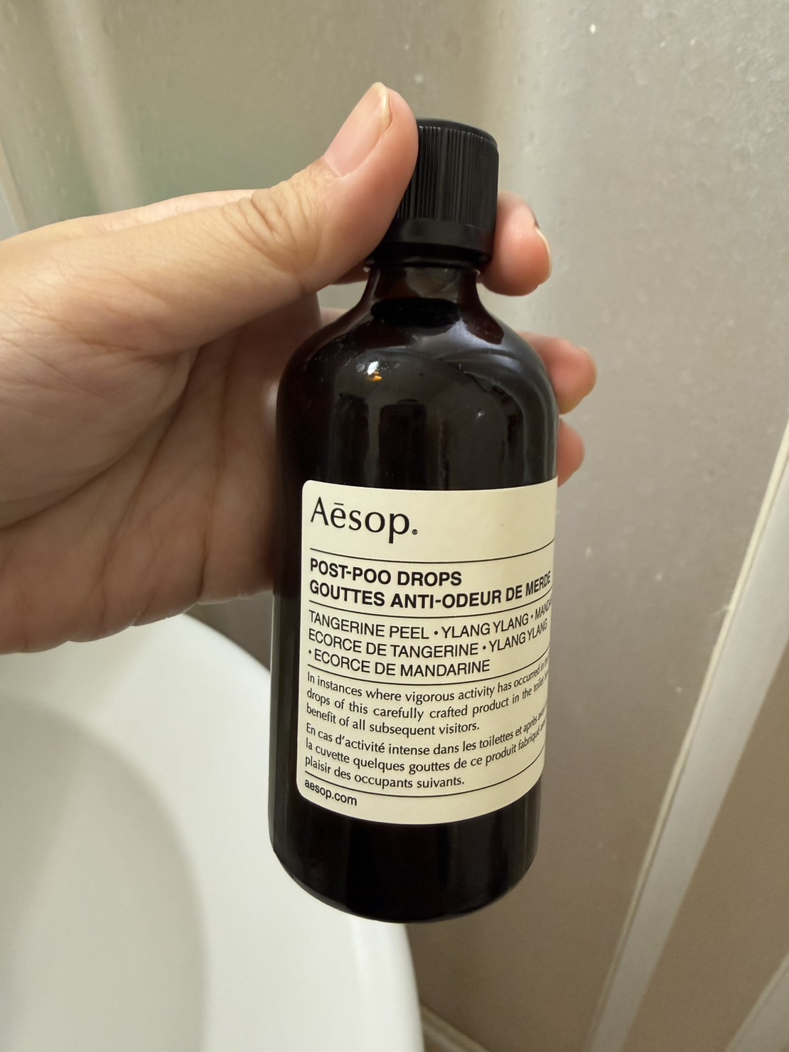 瓶身正面標籤。Aesop／POST-POO DROPS／GOUTTES ANTI-ODEUR DE MERDE，下方是香調與英法雙語說明。
