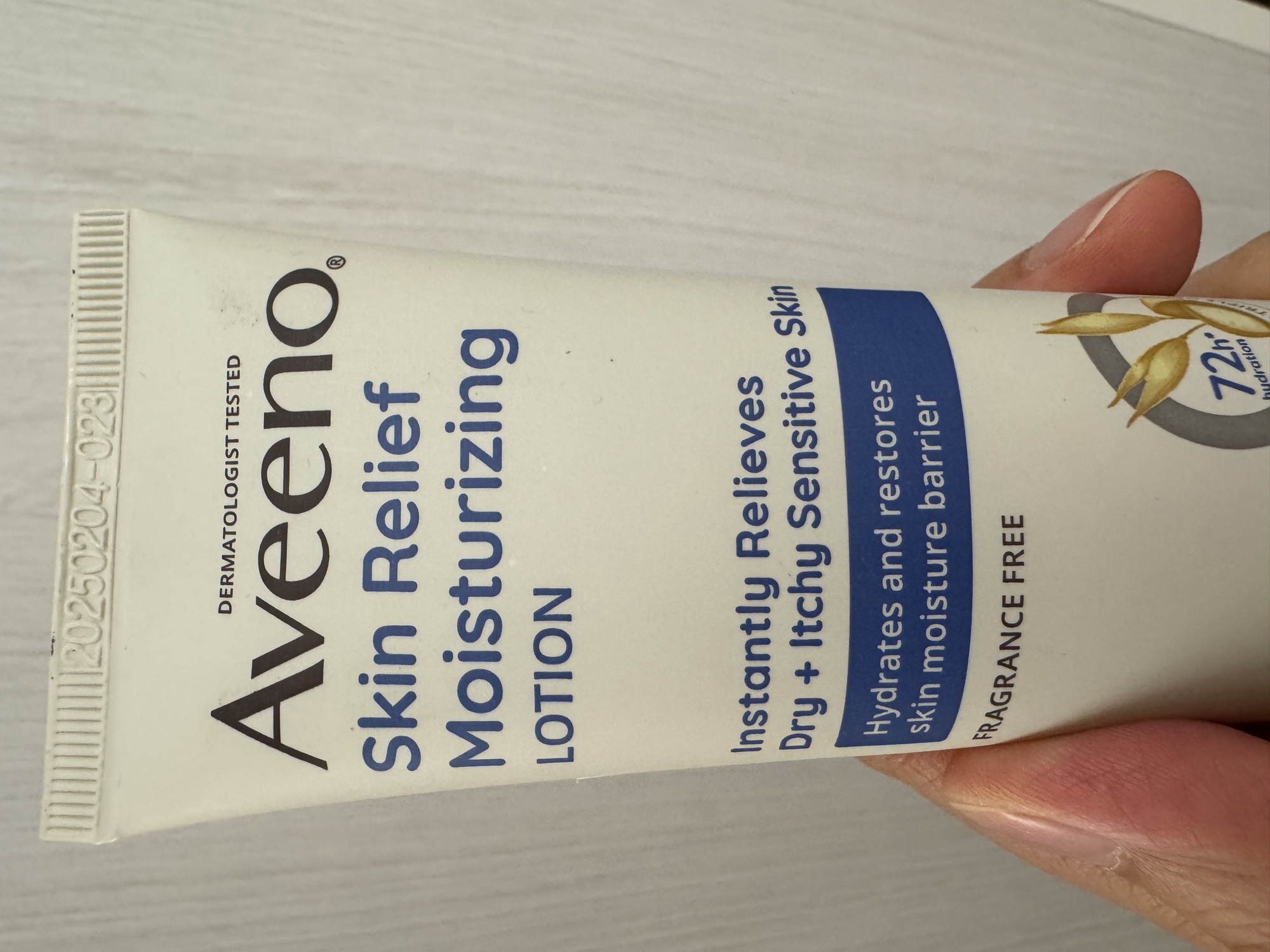 管身正面手持。DERMATOLOGIST TESTED、Skin Relief Moisturizing LOTION、FRAGRANCE FREE，封口壓紋看得到批號。